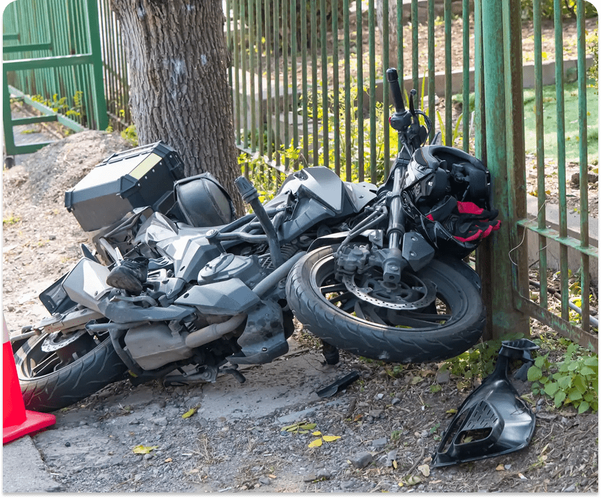 Wrecked motorcycle leaning against fence and tree