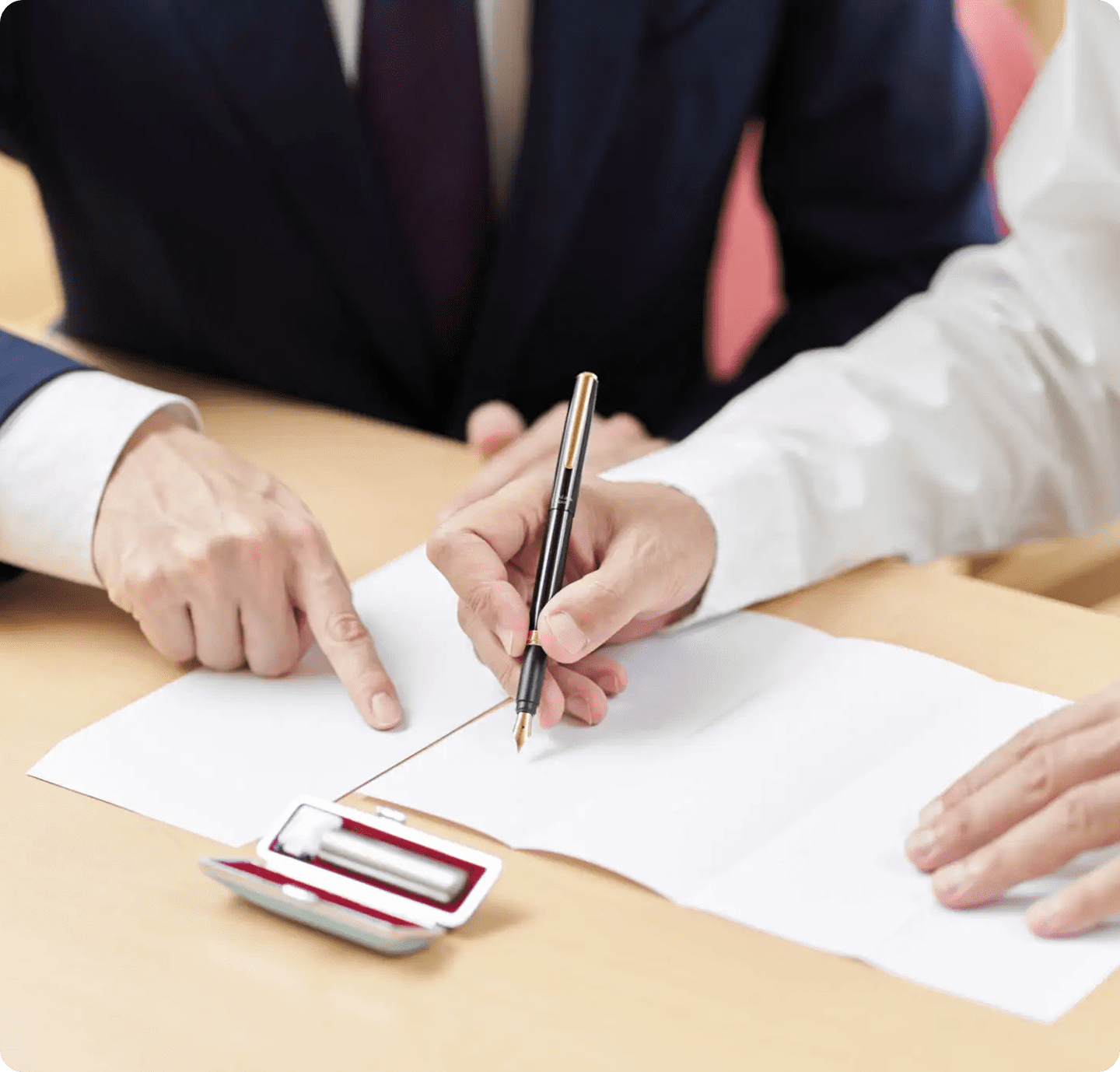 Two professionals signing contract beside ink stamp