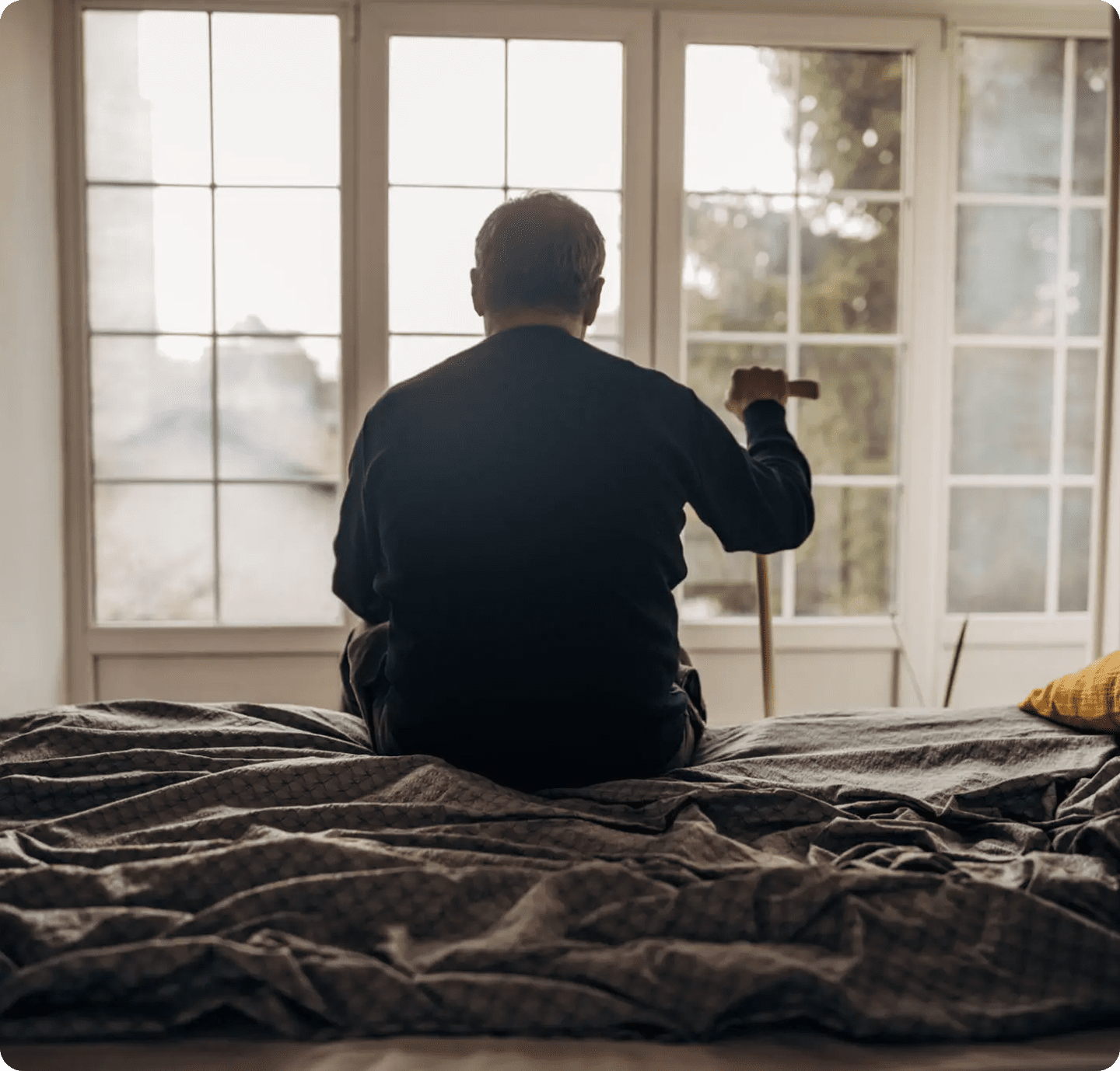 Elderly man with cane sitting, looking out window